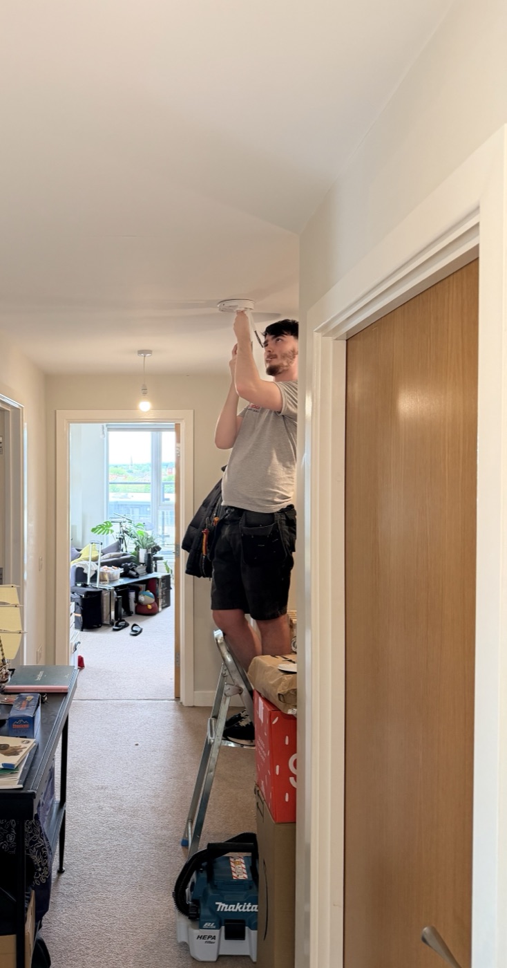 Fire Sure engineer testing a ceiling smoke alarm on a step ladder in a Greater Manchester flat
